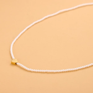 Primer plano de un collar de perlas blancas con un colgante de corazón dorado central
