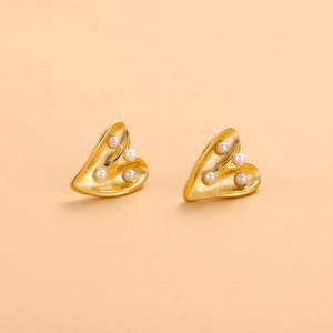 Détail de boucles d'oreilles cœur dorées avec quatre perles blanches sur métal mat