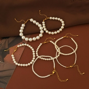 Eleganti bracciali di perle bianche con chiusure dorate su sfondo di pelle marrone scuro