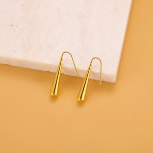 Makro-Detail von glänzenden goldenen Tropfenohrringen auf weißem Marmor mit Licht