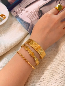 Detailed view of gold irregular stackable bracelets and wide ring on a white fabric background