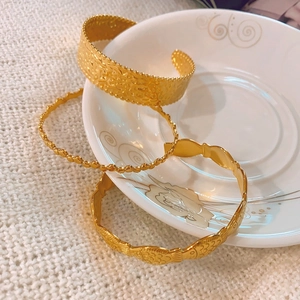 Three gold stainless steel bracelets with hammered texture and bead details on a ceramic dish