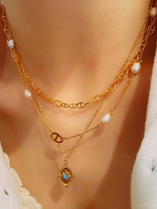 Detail of layered gold necklace featuring a blue gemstone pendant and pearl accents