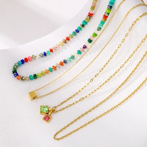 Colorful beaded and gold layered necklaces set with square charms on white surface