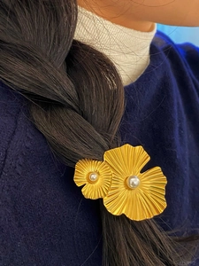 Dettaglio di un fermaglio per capelli a doppia fiore dorato con perle su treccia