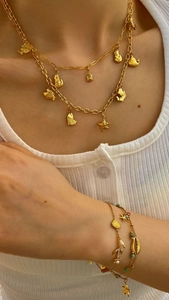 Dettaglio di collane e bracciali dorati a strati con ciondoli marini indossati sul corpo