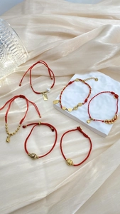 Detaillierte Nahaufnahme roter Armbänder mit Goldanhängern auf elegantem Seidenhintergrund