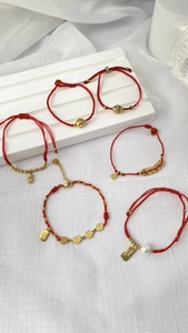 Detail von roten geflochtenen Armbändern mit goldenen Münzen und Glückssymbolen