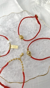 Nahaufnahme roter Flechtarmbänder mit goldenen Glücksbringern, Perlen und Anhängern