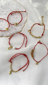 Detail von roten geflochtenen Armbändern mit goldenen Glücksbringern und Perlen