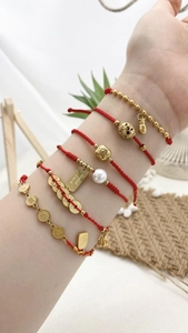 Detailansicht der gewebten roten Schnurarmbänder mit goldenen Glücksbringern und Perlen