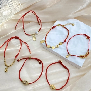 Handgewebte rote Armbänder mit goldenen Glücksbringern auf Champagner-Satin und Stein