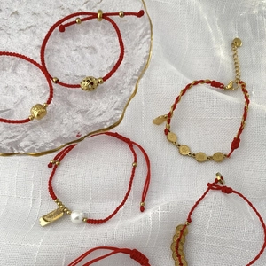 Rote geflochtene Armbänder mit goldenen Glücksbringern und Perlen auf Glastablett
