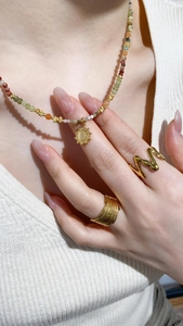 Detail of colorful seed pearl necklace with gold sun pendant and textured gold rings