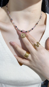 Close-up of a French style pearl necklace with gold pendant and layered leaf textured rings