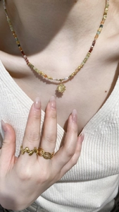 Close-up of pearl bead necklace with sun pendant and matching gold rings on a model