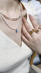 Close-up of layered pearl necklace with blue gemstone and gold-plated floral rings