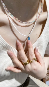 Detail of layered gold necklaces with pearl pendant and gemstone alongside butterfly rings