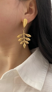 Close-up of elegant gold leaf drop earrings worn by a model in a minimalist style