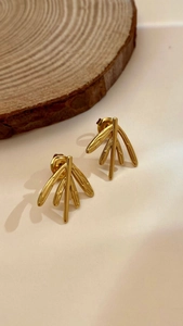 Detailed view of gold branch-shaped earrings on a rustic wood slice with a natural finish