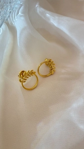 Detailed view of golden leaf earrings on white silk fabric with elegant glass props