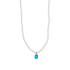 Detailed view of tiny white pearls and a blue rectangular gemstone pendant on a gold necklace