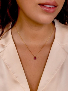 Close-up of elegant gold chain necklace with teardrop red gemstone on model