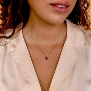 Close-up of a pear-shaped red gemstone pendant on a gold chain worn by a model