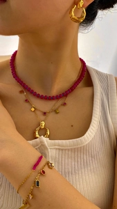 Detail of layered gold necklaces with red beads and colorful pendant on model neck