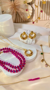 Detailed close-up of beaded necklaces and gold earrings on white silk fabric background