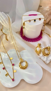 Detailed set of gold tone jewelry with pink beads and organic charms on white props