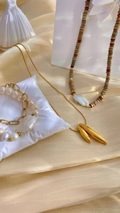 Dettaglio di collane con perle barocche e bracciali dorati su raso color champagne