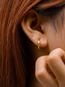Close-up of minimalist gold geometric heart hoop earrings worn on a model's earlobe