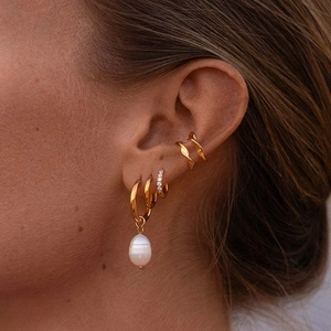 Gold earring set with hoop, drop pearl charm, and twisted ear cuff on model ear