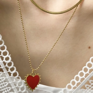 Dettaglio di una collana dorata a due strati con ciondolo a cuore rosso e bordo in pizzo