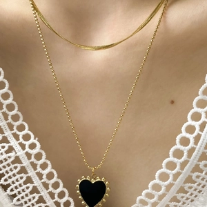 Dettaglio collana dorata a due strati con catena a serpente e ciondolo cuore nero