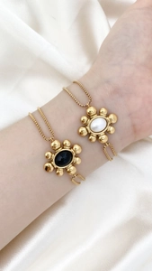 Detail eines Vintage-Blumenarmbands mit schwarz-weißen Emaille-Anhängern an Goldkette