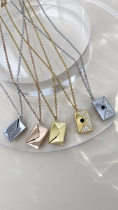 Detalle de colgantes de sobre en oro y plata con circonitas sobre base acrílica