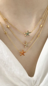 Close-up of triple-layered gold star and starfish necklaces with colorful crystal pavé