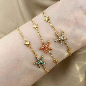 Golden starfish bracelets with blue orange and white crystal charms on a model wrist