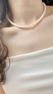 Detail of elegant pearl bead choker on woman's neck wearing white silk shirt