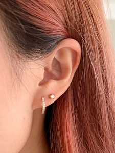 Gros plan sur une boucle d'oreille créole dorée et un clou en zircon sur l'oreille