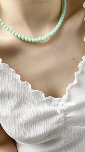 Close-up of light green beaded necklace on a model wearing a white pleated blouse