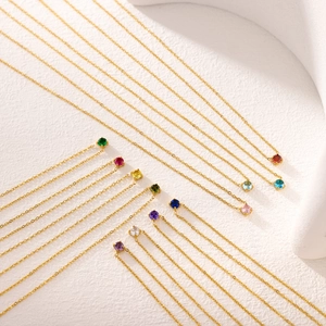 Détail de colliers chaîne croisée dorés avec des pendentifs ronds en zircons colorés