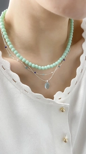 Close-up of elegant triple-layered necklace with pale green beads and oval blue pendant