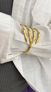 Detail of a polished gold skeleton hand bangle styled over a white linen sleeve cuff