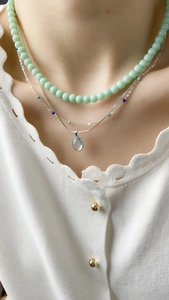 Close-up of layered necklaces featuring light green beads and silver pendant details