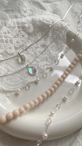 Detail of luxury pendant necklaces on white ceramic tray and lace in a soft-toned composition