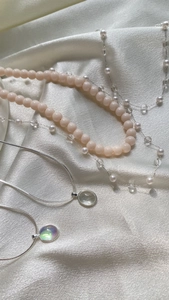 Detail of luxury necklaces with pink beads and opal pendants on white satin fabric