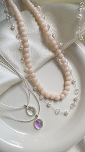 Close-up of layered pearl necklace and silver chain with purple crystal pendants